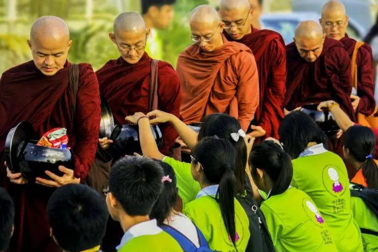 Buddhist monks in saffron robes receiving offerings from children in a peaceful ceremony.