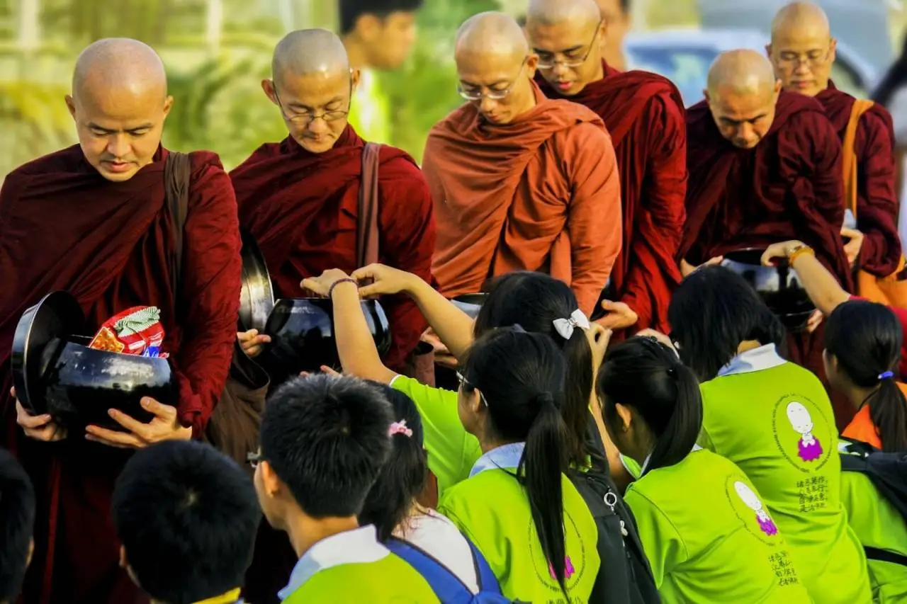 Buddhist monks in saffron robes receiving offerings from children in a peaceful ceremony.