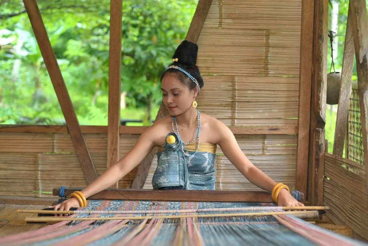 Woman weaving traditional fabric on a loom, showcasing cultural attire.